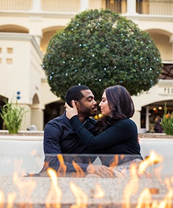 A couple turning in to kiss outside next to a fire.