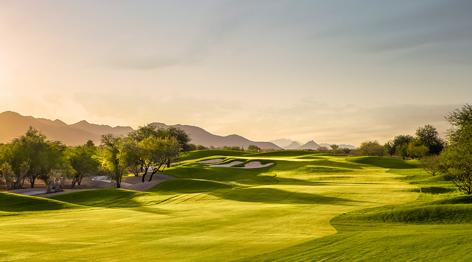a golf course with trees and mountains in the background