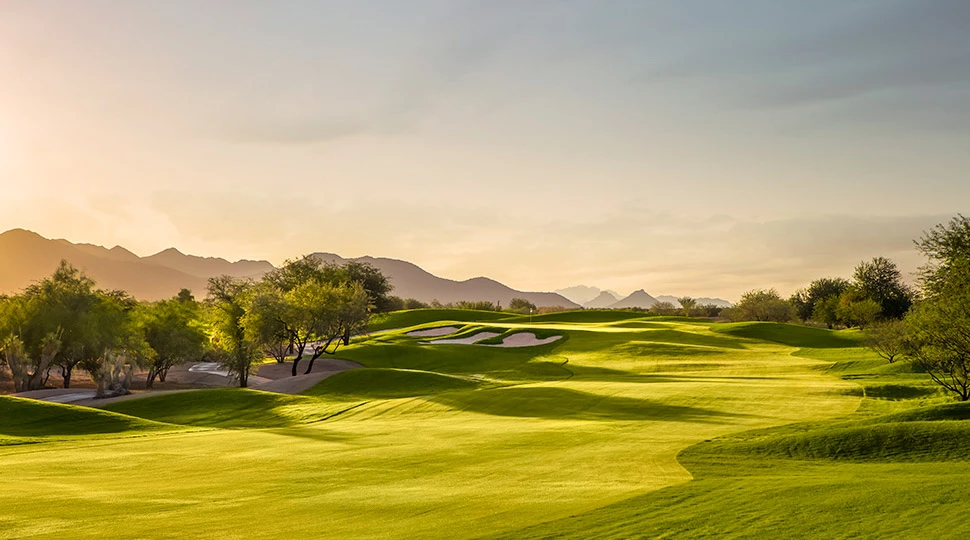 a golf course with trees and mountains in the background