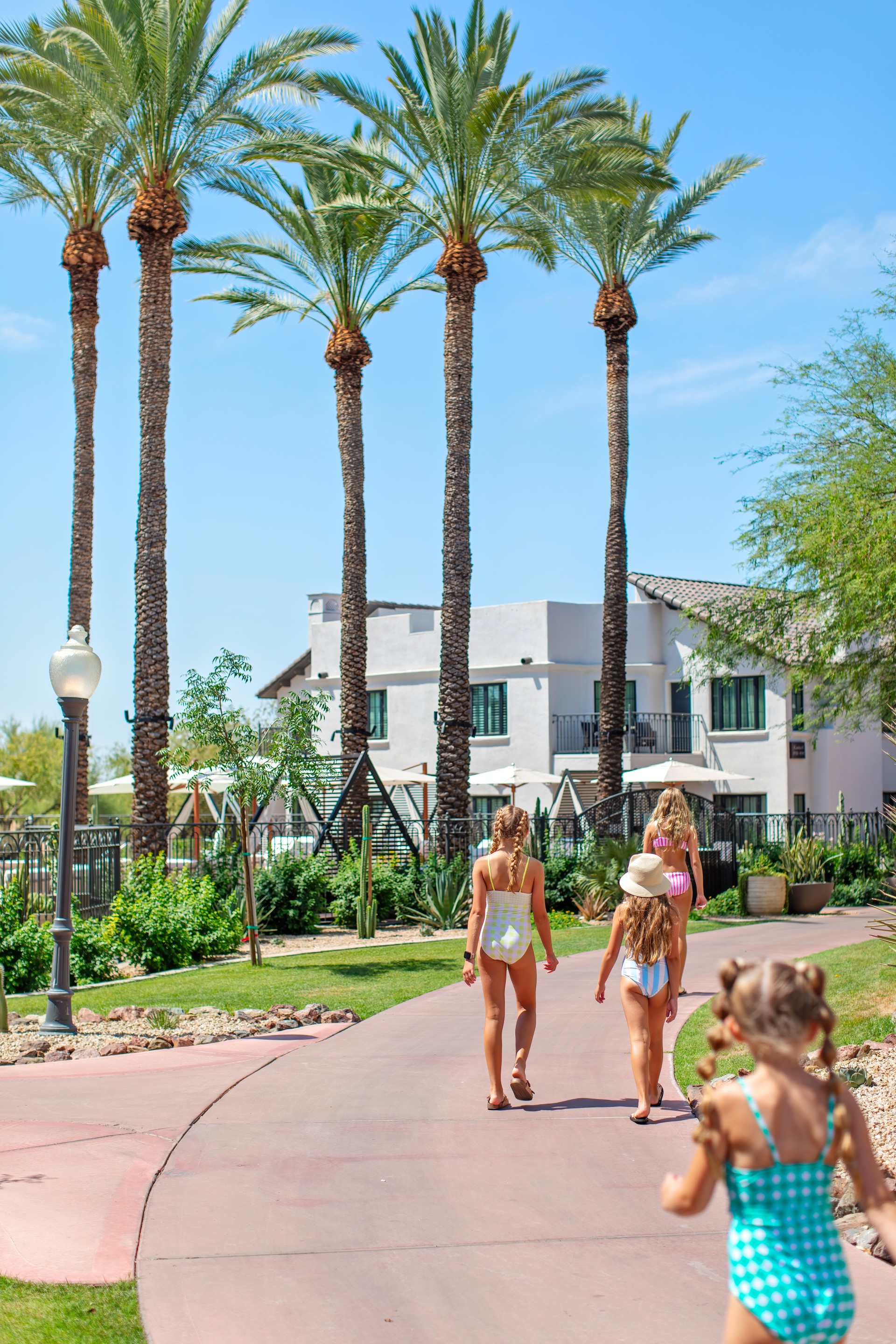 a group of girls in swimsuits walking down a sidewalk with palm trees