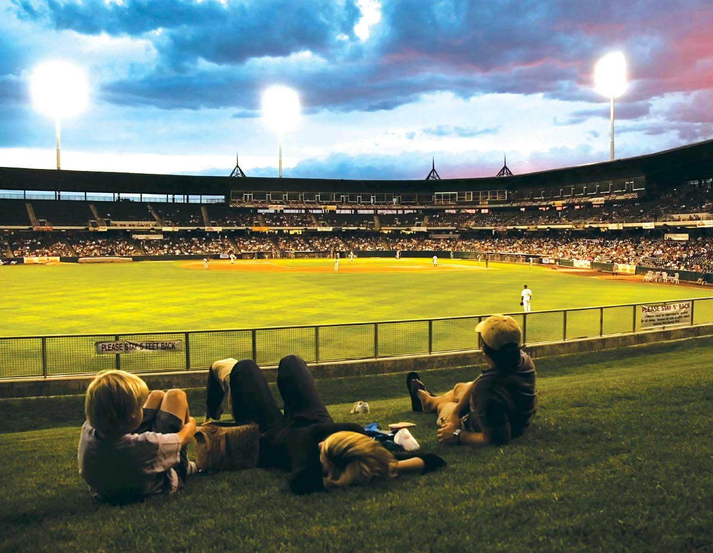 people sitting on the grass in a baseball stadium