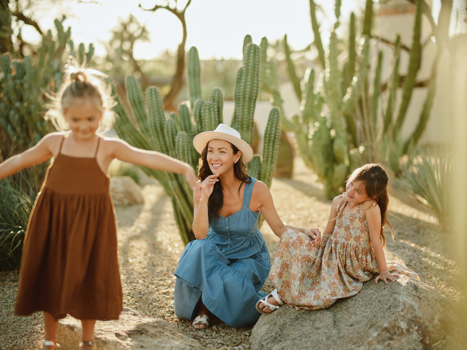 a woman and two girls sitting on a rock in a cactus garden
