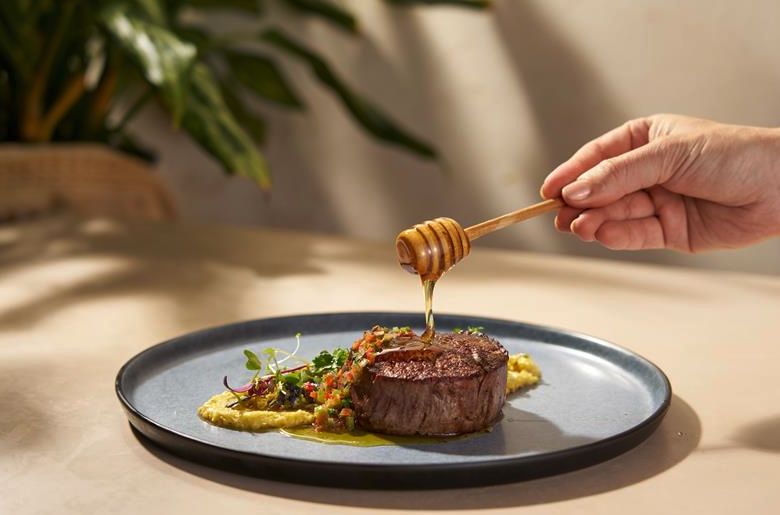 a person pouring honey onto a piece of meat on a plate