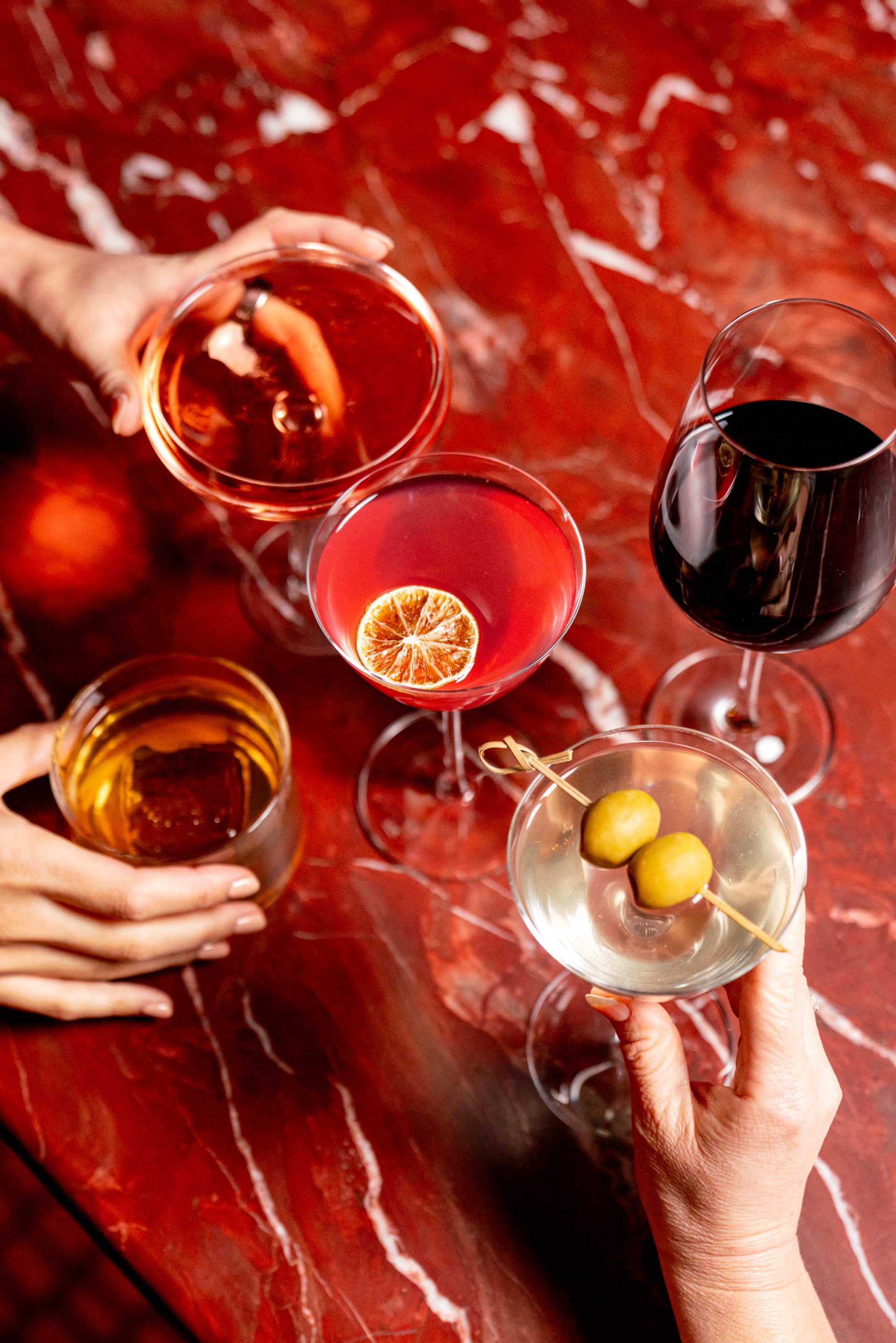a group of hands holding glasses of different colored drinks