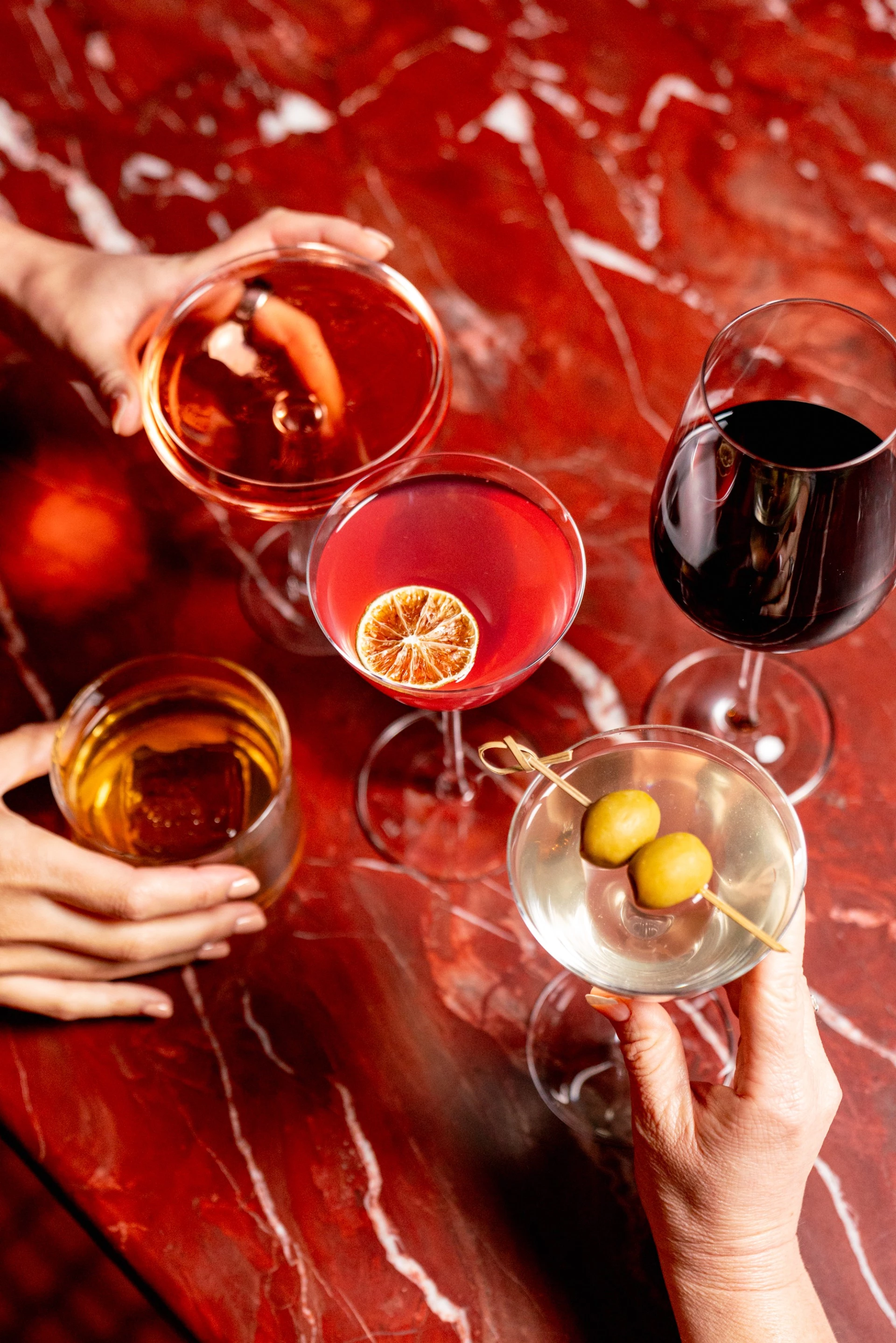 a group of hands holding glasses of different colored drinks