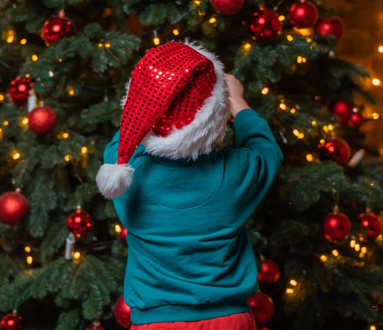 a child wearing a santa hat and standing by a christmas tree