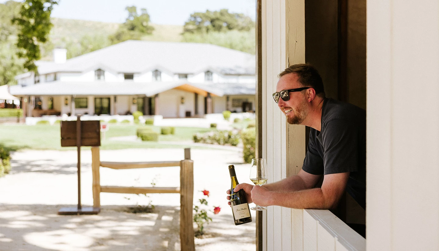a man holding a bottle of wine and looking out a window