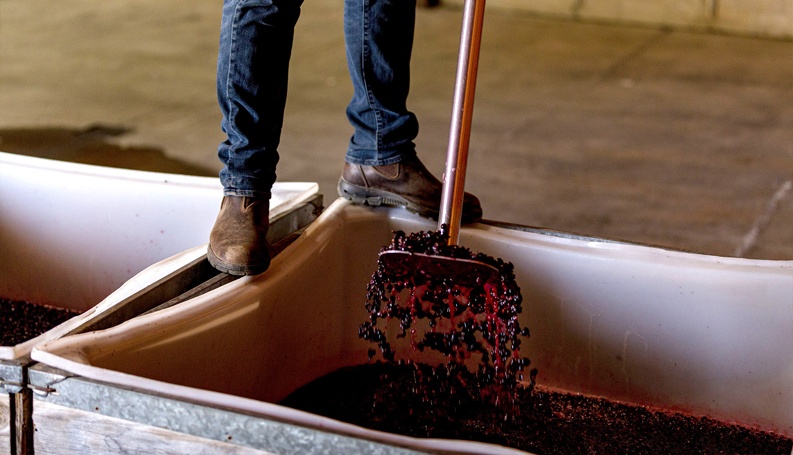 a person holding a broom over a container of wine