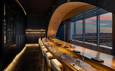 a long table with wine glasses and chairs in a room with a view of the mountains