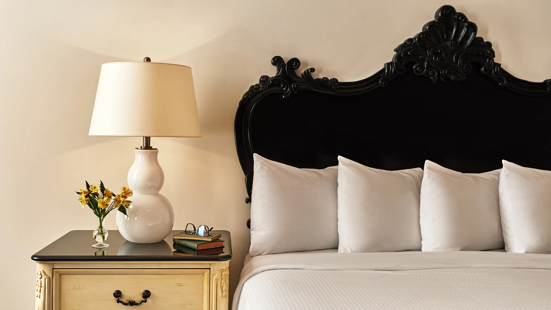 a white bed with a lamp and a vase of flowers on a nightstand