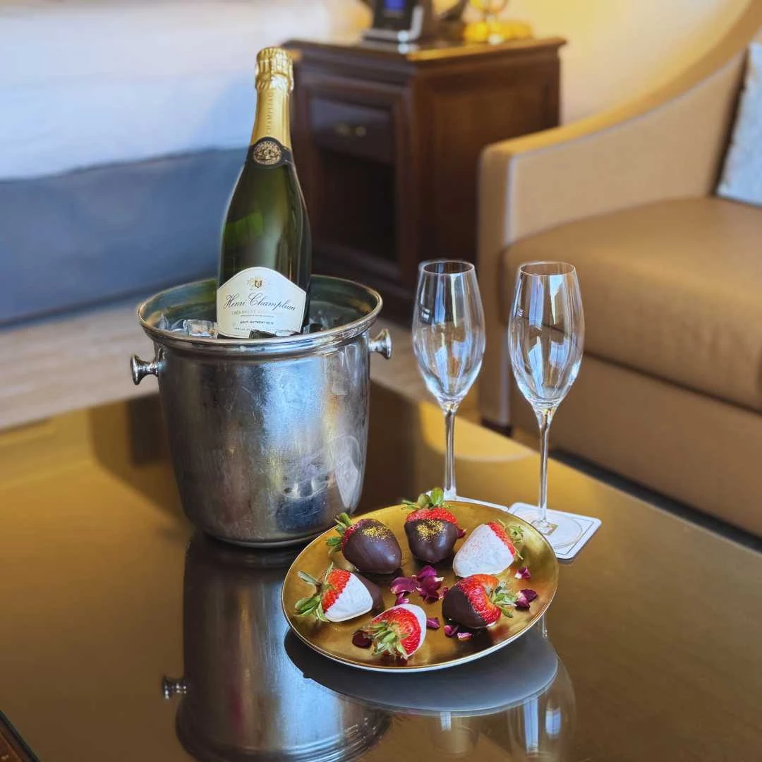 a champagne bottle in a bucket with a plate of strawberries and two wine glasses on a table