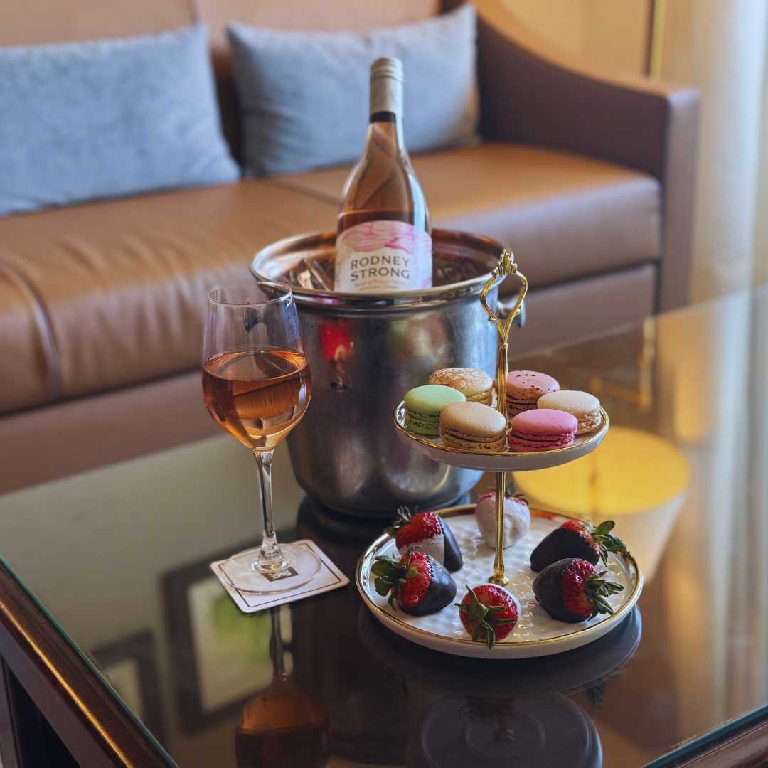 a glass of wine and a tray of strawberries and macaroons on a table