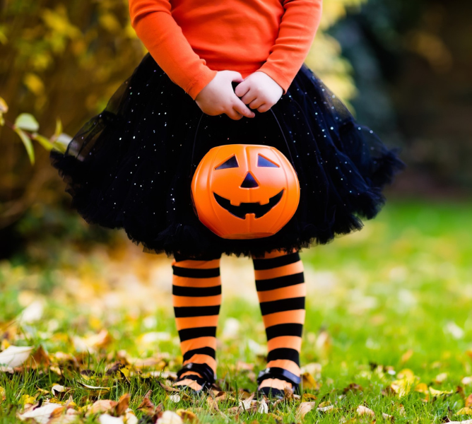 a child wearing a tutu and a black and orange outfit holding a pumpkin bucket