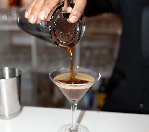 a person pouring a drink into a martini glass