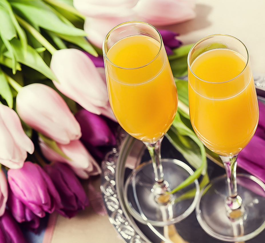 two glasses of orange juice next to a bouquet of tulips