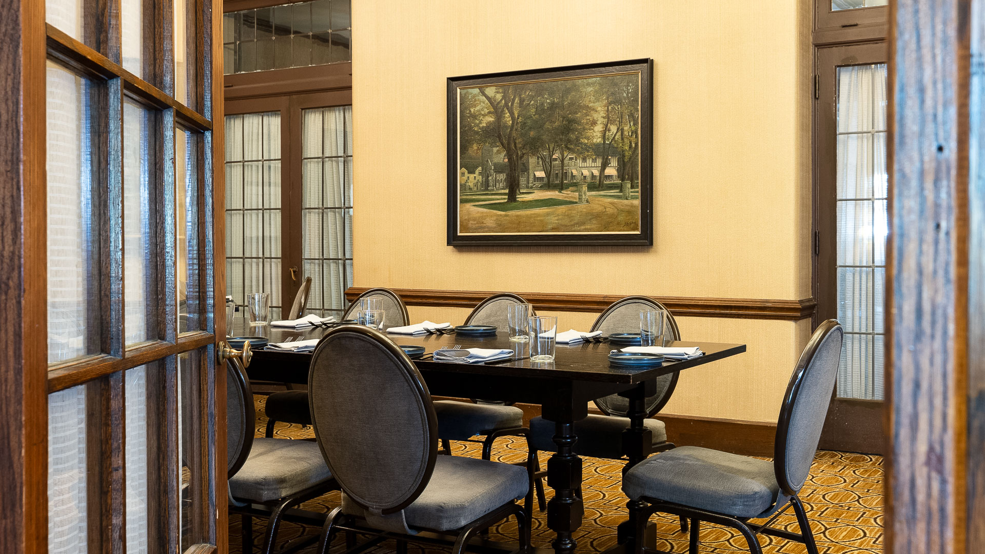 a table set up for dinner with chairs and a painting on the wall