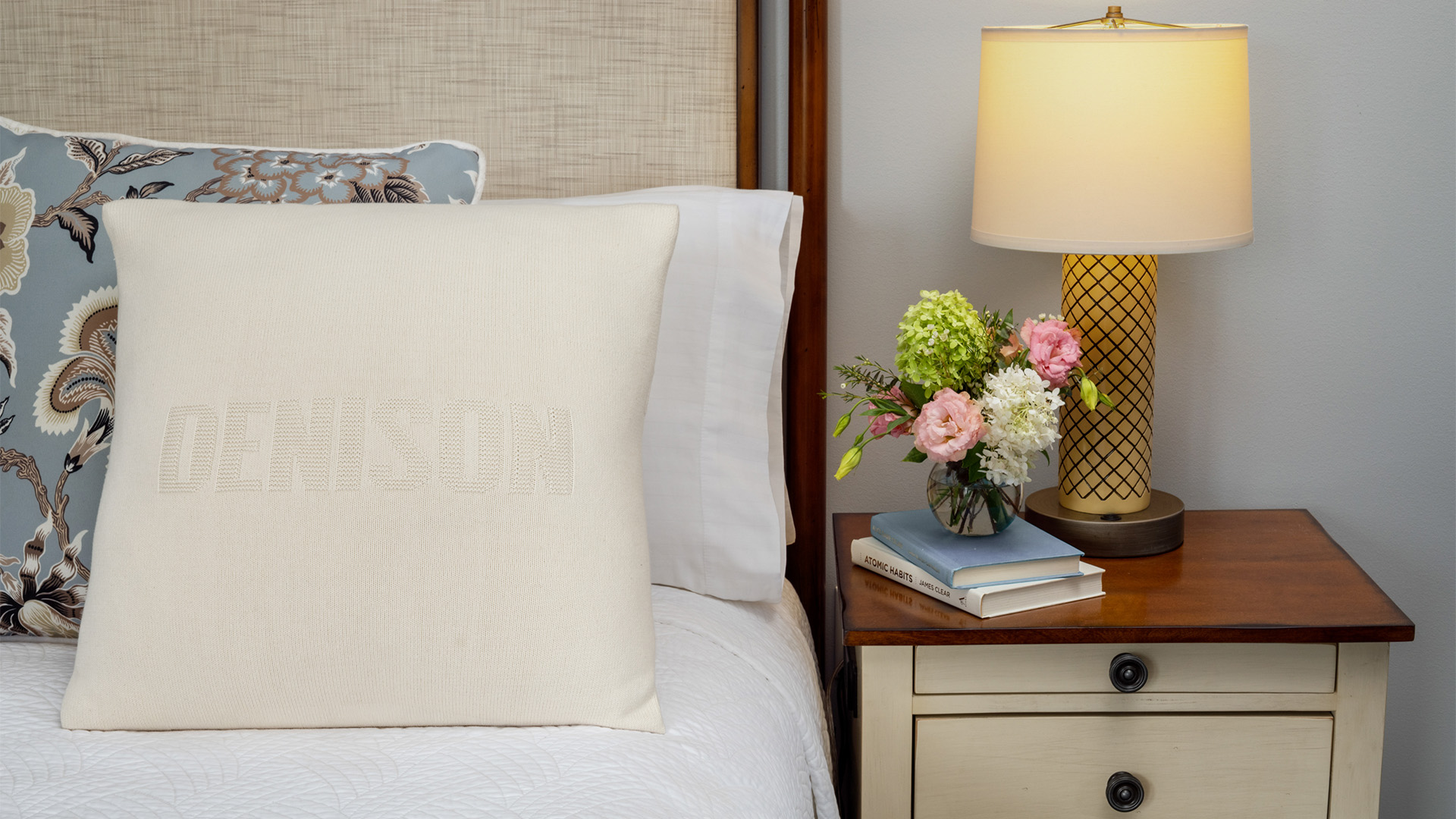 a white pillow on a bed next to a table with flowers