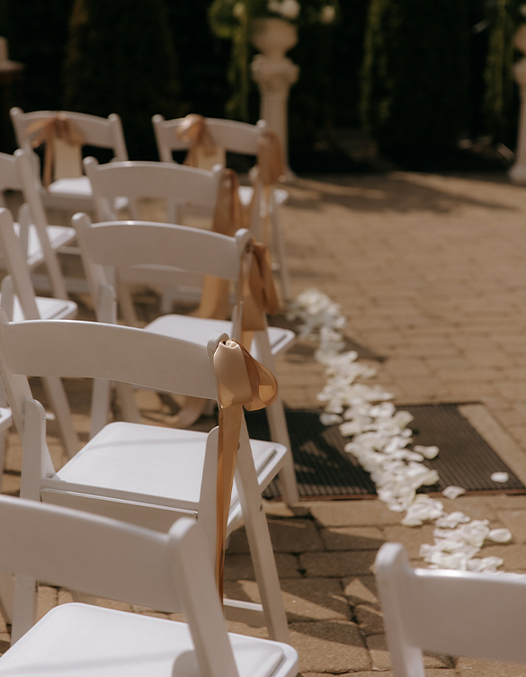 a row of white chairs with gold ribbons