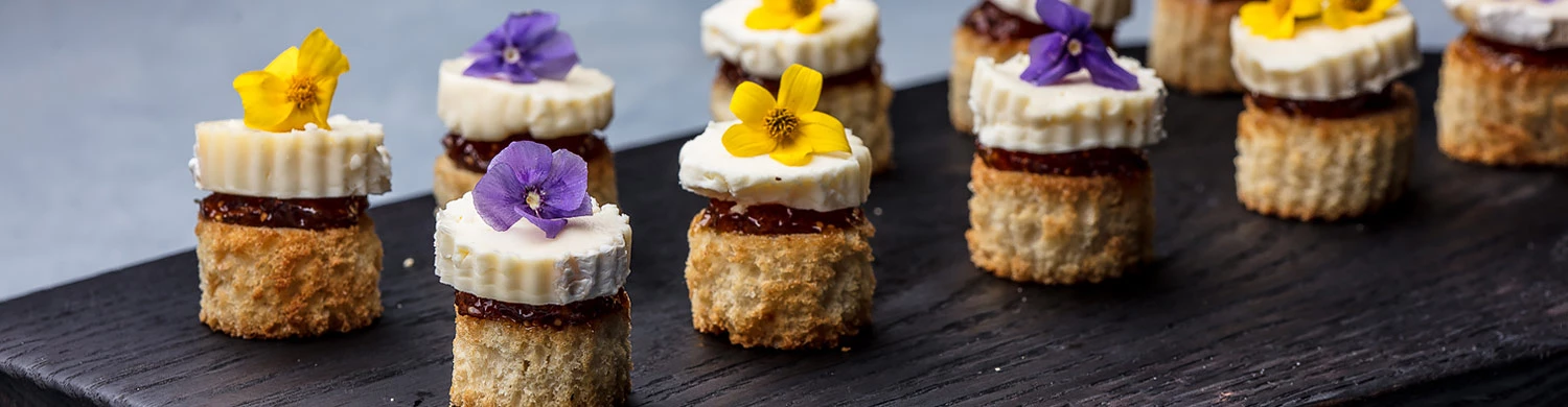 small pastry appetizers on a plate garnished with yellow and purple flowers