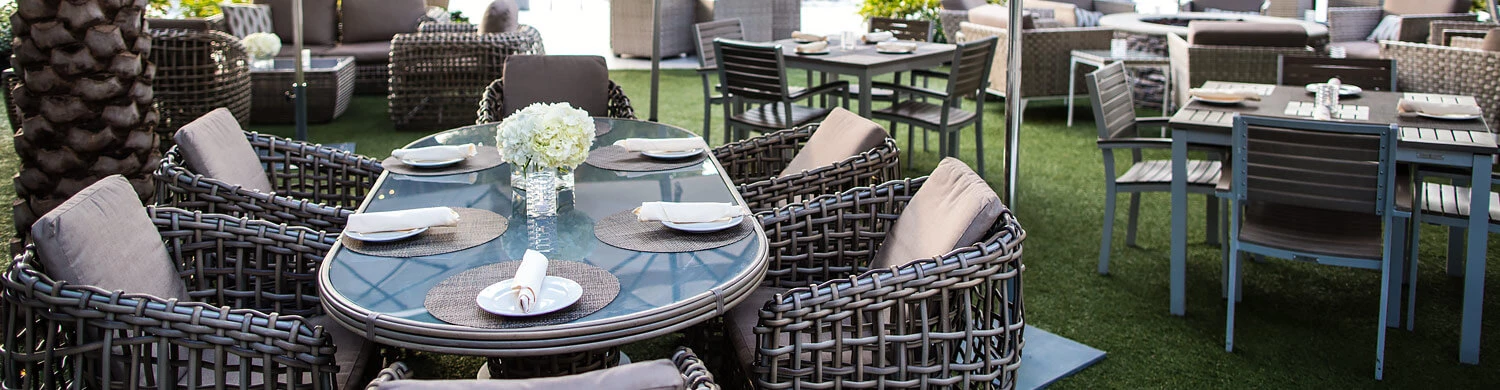 a long rounded glass outdoor dining table set surrounded by cushioned wicker chairs on a grass patio