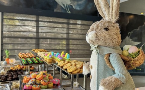 a stuffed bunny rabbit with a basket of eggs on a table of pastries