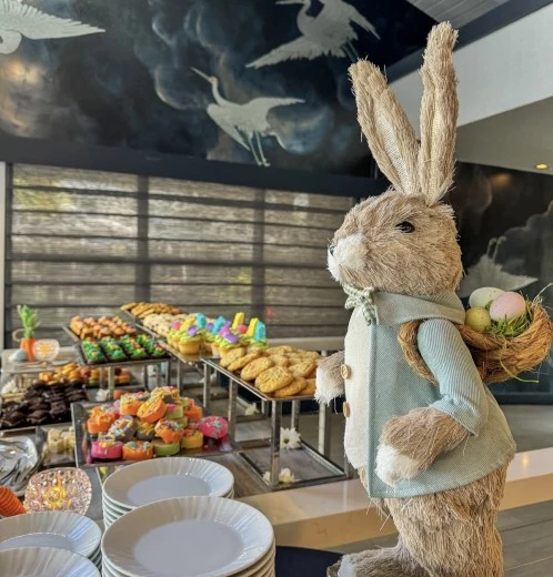 a stuffed bunny rabbit with a basket of eggs on a table of pastries