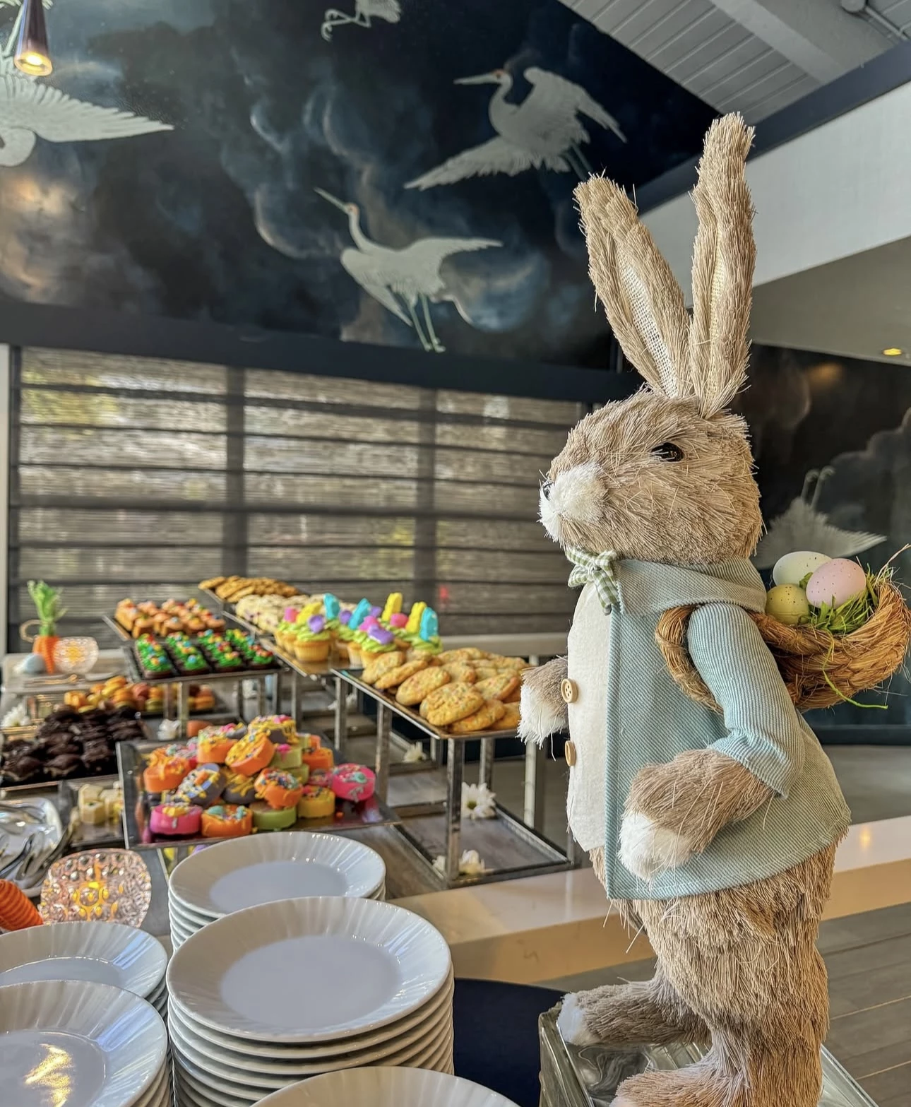 a stuffed bunny rabbit with a basket of eggs on a table of pastries