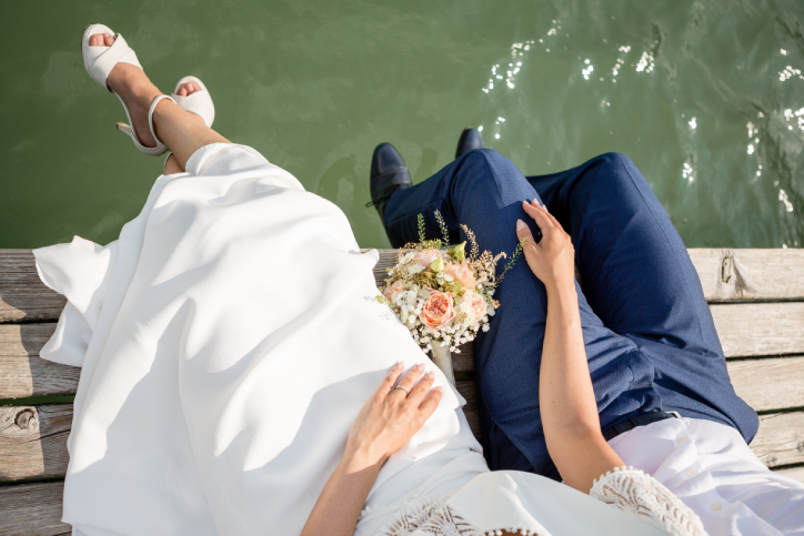 bride and groom sitting on wooden ledge over lake