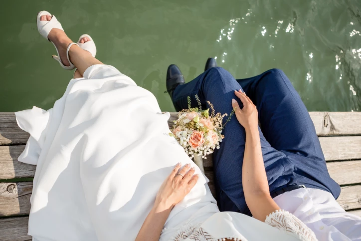bride and groom sitting on wooden ledge over lake