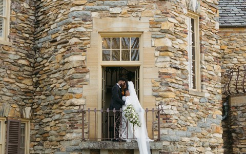 a man and woman standing on a balcony in front of a stone building