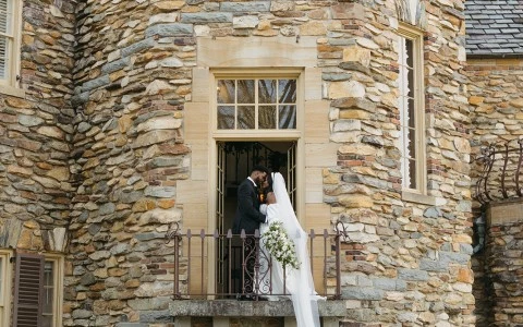 a man and woman standing on a balcony in front of a stone building