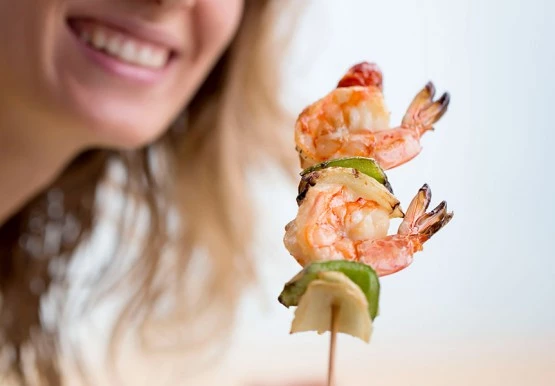 Woman holding wooden skewer with shrimp, onion & pepper 