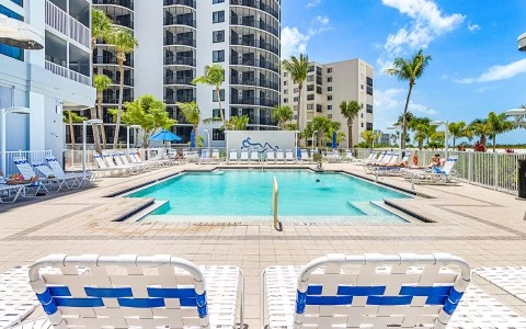 a pool with chairs and palm trees in front of a building