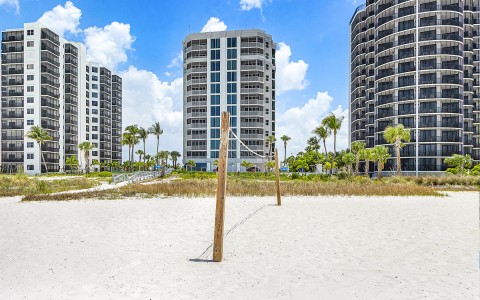 a beach volleyball net in sand with tall buildings in the background