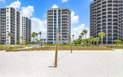 a beach volleyball net in sand with tall buildings in the background