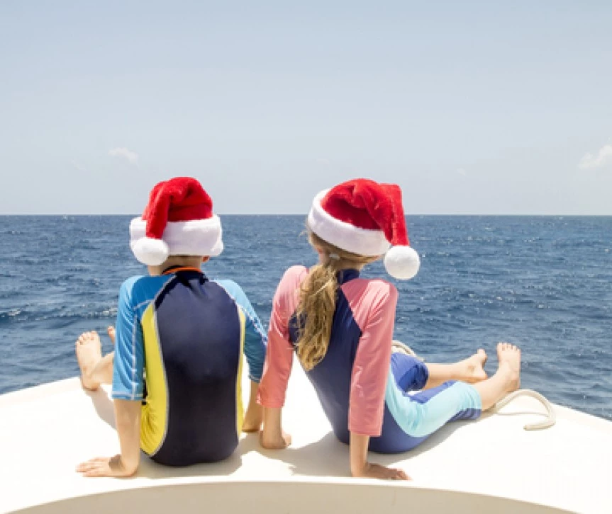 two kids on the bow of a boat wearing santa hats