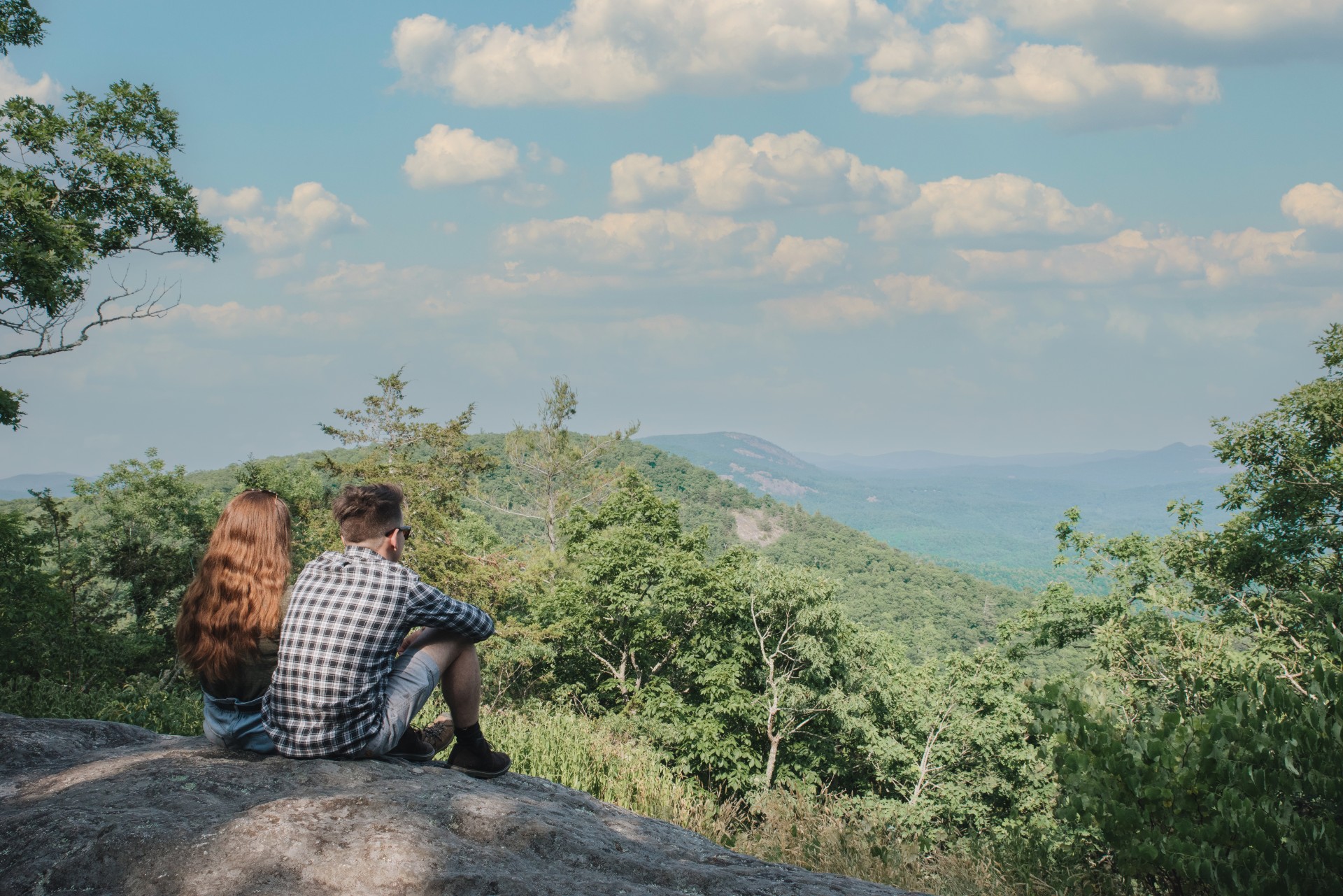 a man and woman sitting on a rock looking at a valley