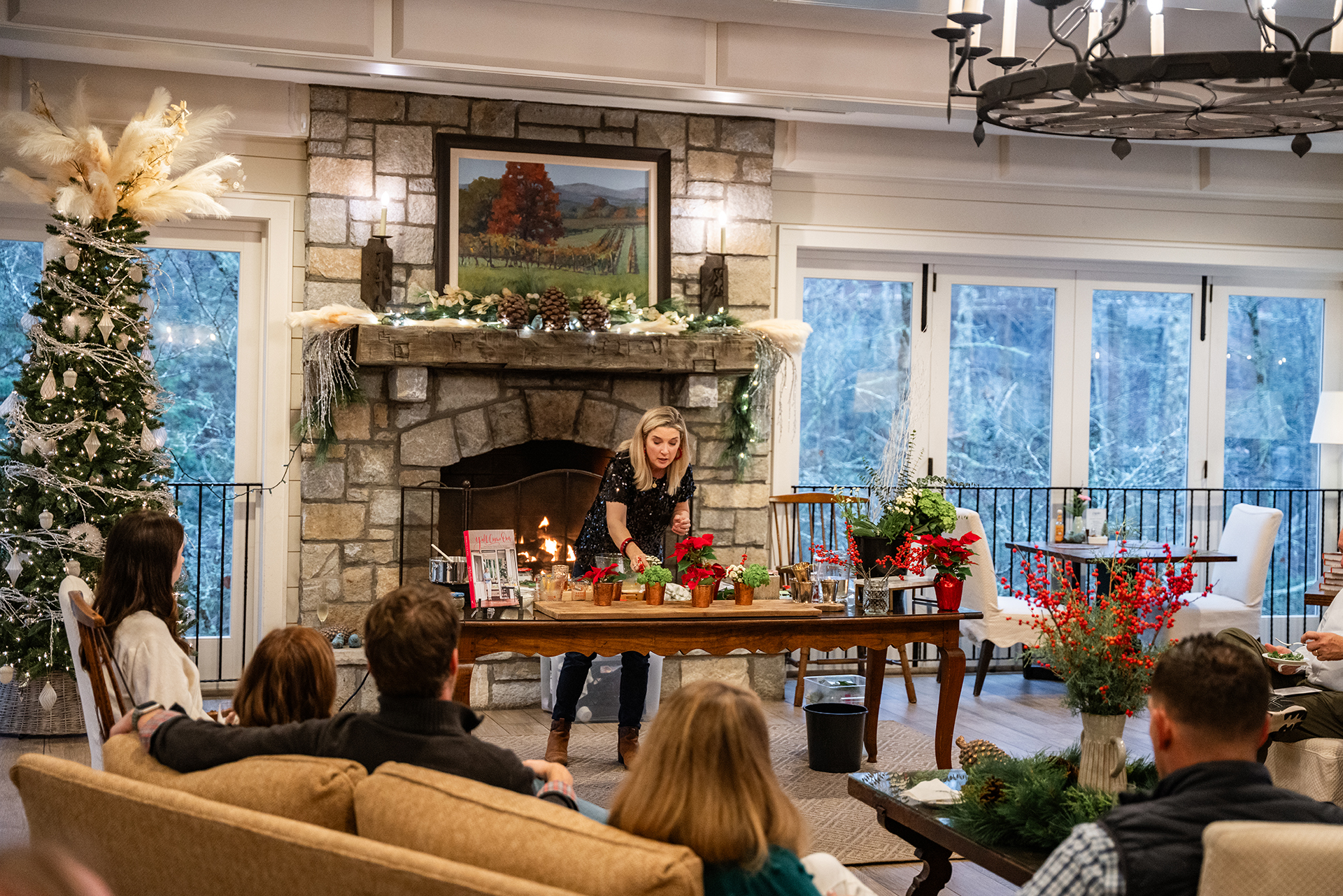 a woman standing in front of a fireplace with people sitting on couches