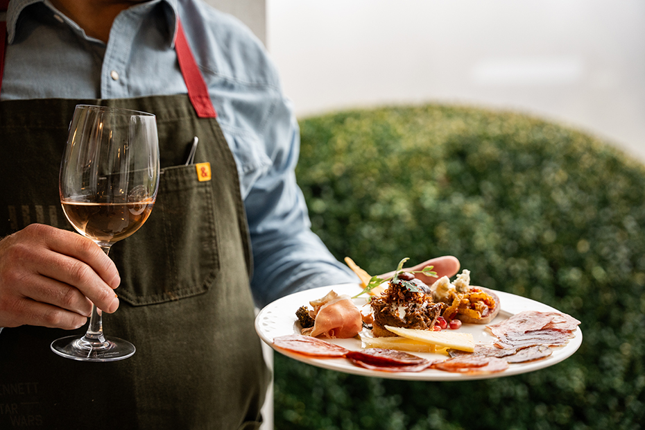 a person holding a plate of food and a glass of wine