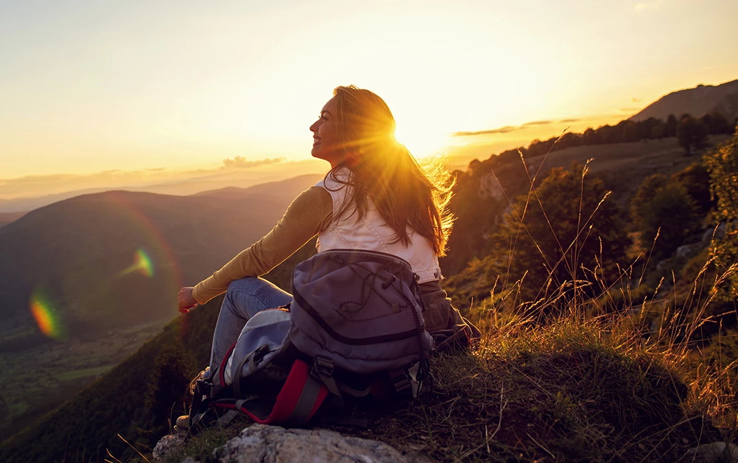 a woman sitting on a rock looking at the sunset