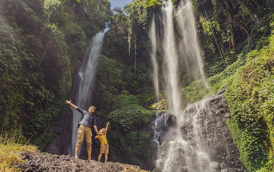 a man and child standing on a rock in front of a waterfall