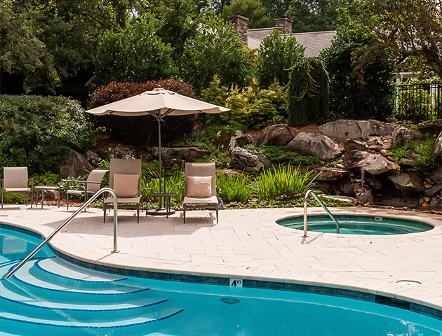 a pool with chairs and umbrella by a house