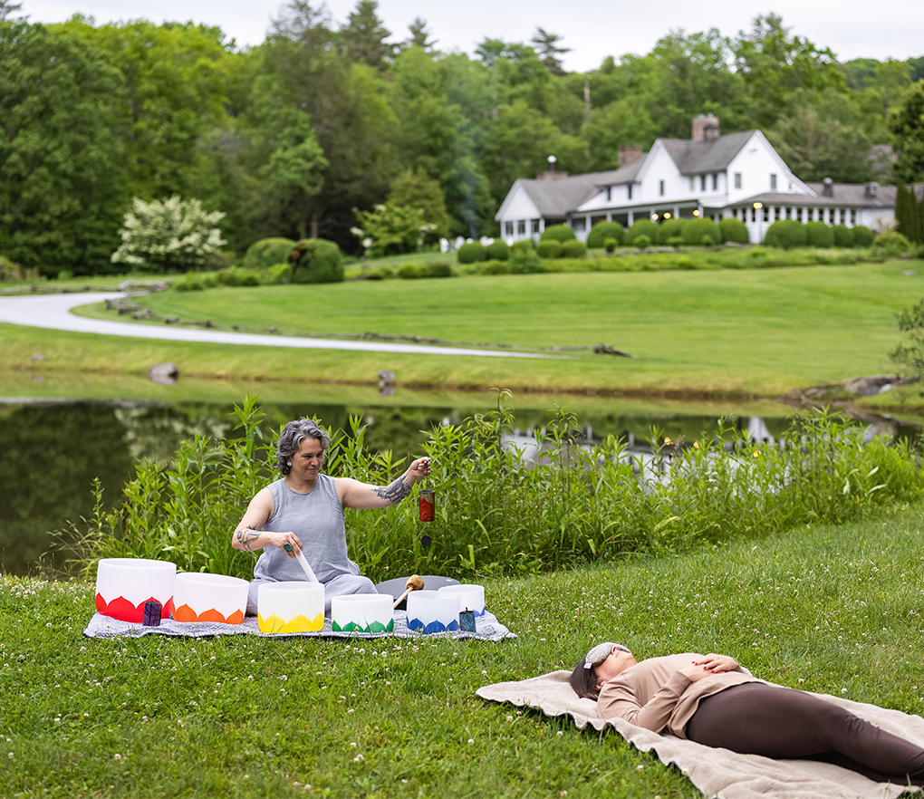 a woman sitting on a blanket in a grassy area next to a lake