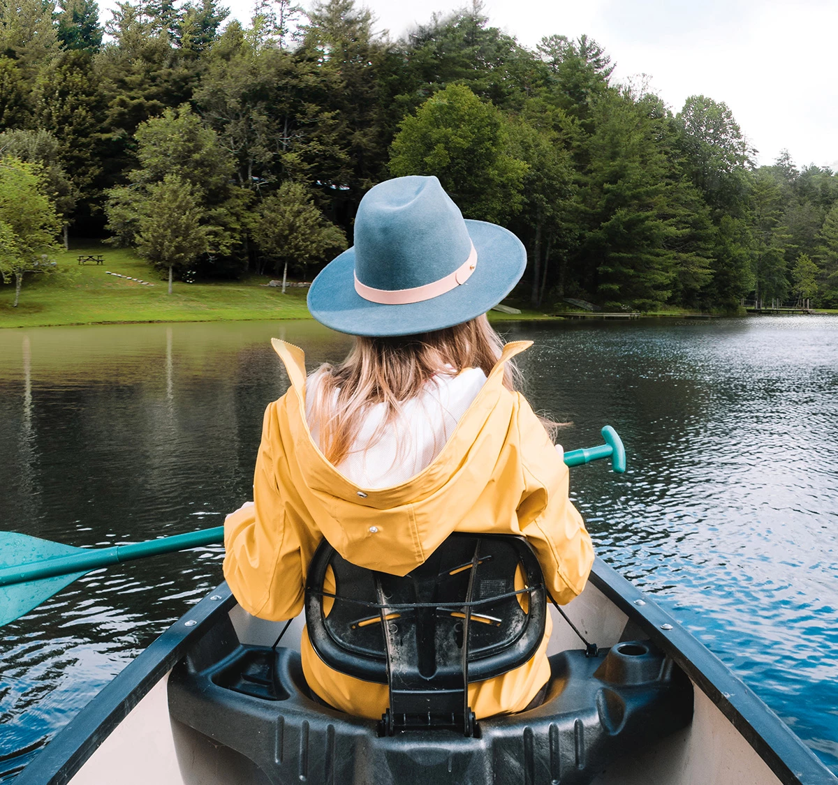 a woman in a yellow jacket and hat rowing a boat on a lake