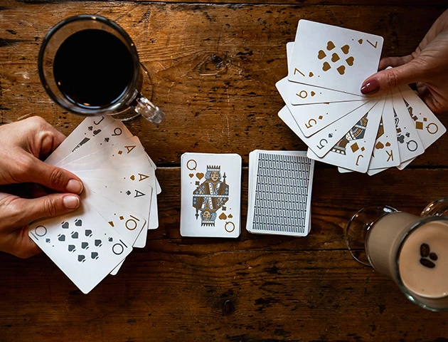 a person holding cards and a glass of beer