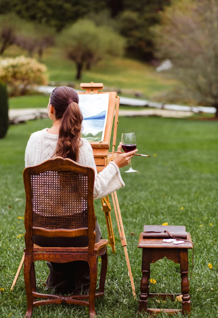 a woman painting on an easel in a grass field