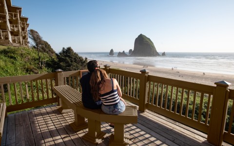 a man and woman sitting on a bench overlooking a beach