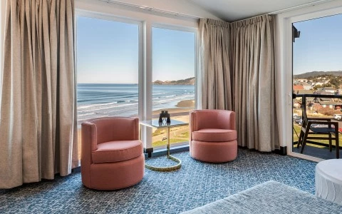 a room with two pink chairs and a table with a view of the ocean