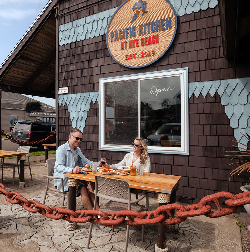 a man and woman sitting at a table outside a restaurant