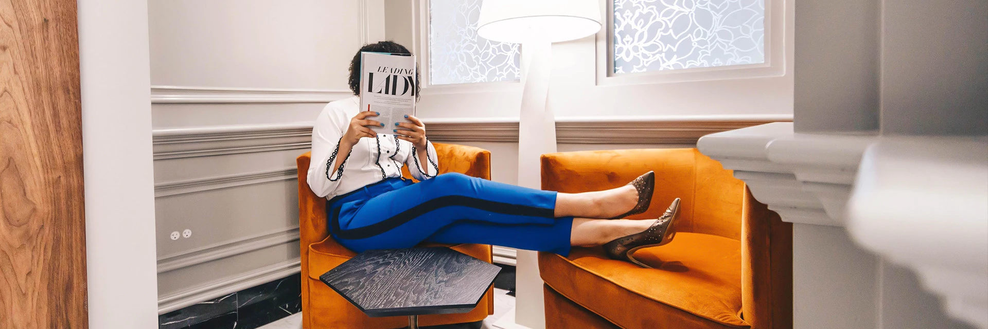 lady sitting in a orange chair reading a paper 